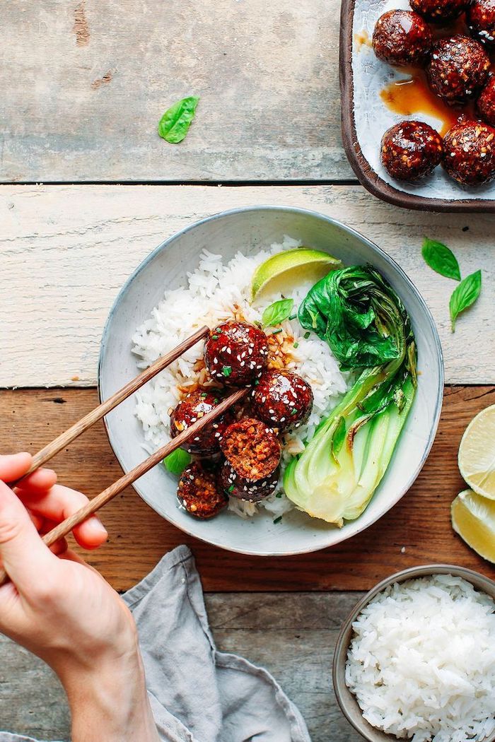 teriyaki meatballs with white sesame seeds vegan party appetizers placed in white rice in white ceramic plate lime wedges on the side