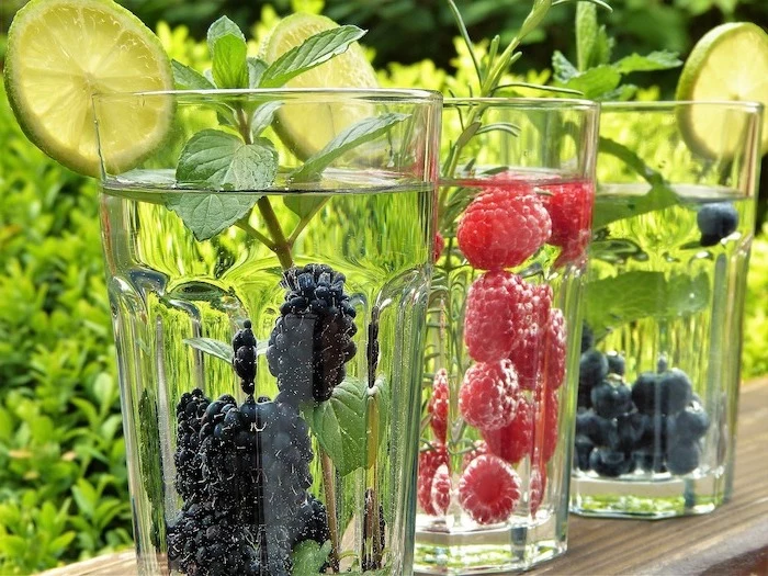 three glasses filled with water best detox drink one glass with blackberries one with raspberries one with blueberries