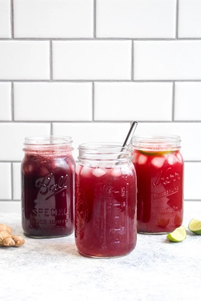 three mason jars filled with red smoothies garnished with lime slices ice how to detox your body ginger and lime on the side