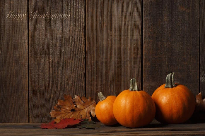 three pumpkin with three fall leaves in brown green orange on wooden surface cute thanksgiving wallpaper