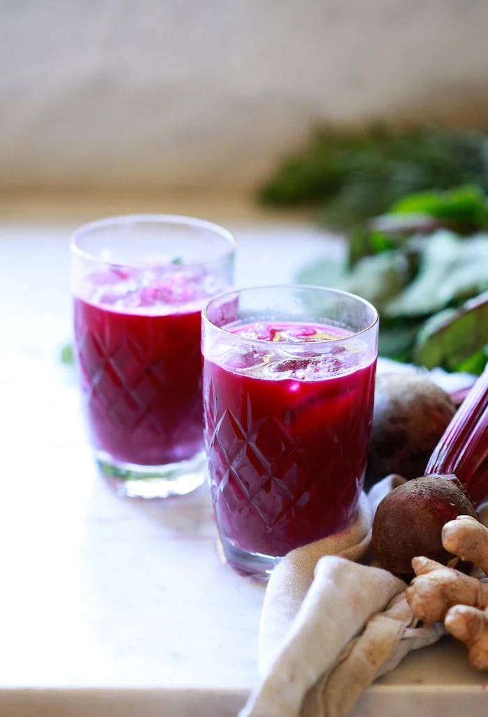 two glasses filled with beet juice placed on marble surface detox drinks for weight loss ginger and beetroot on the side