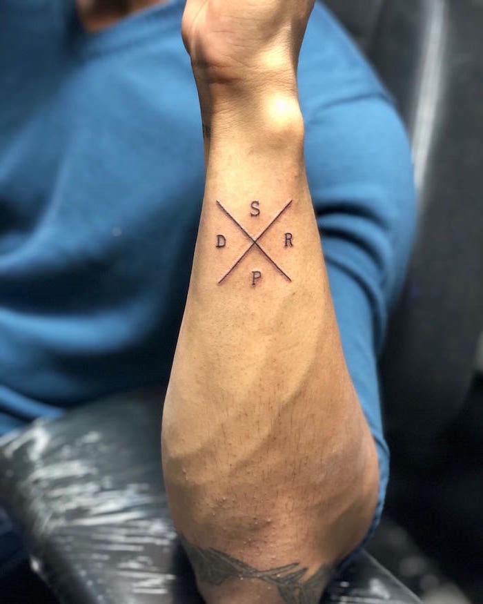 two lines crossing as x small tattoos for men s d p r letters written around them forearm tattoo on man wearing blue blouse