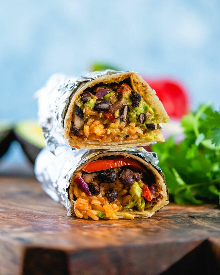 two vegan burritos wrapped in foil placed on wooden cutting board popular mexican food