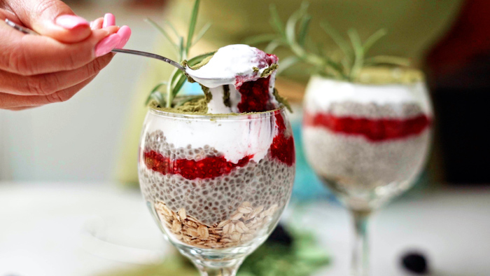 two wine glasses filled with chia pudding topped with matcha powder vegan bites garnished with fresh rosemary