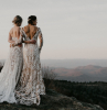 two women wearing all lace white dresses plus size beach wedding dresses photographed standing on a hill hugging