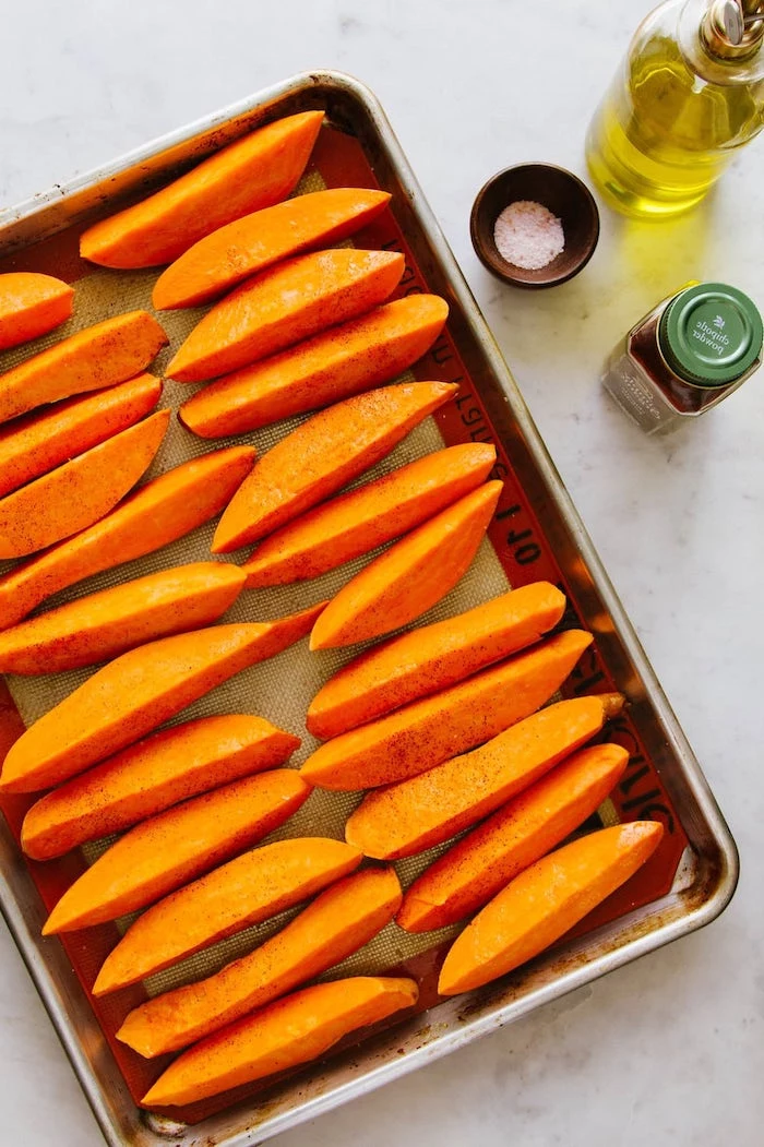 vegan party appetizers sweet potato wedges arranged on paper lined baking sheet covered with salt pepper olive oil
