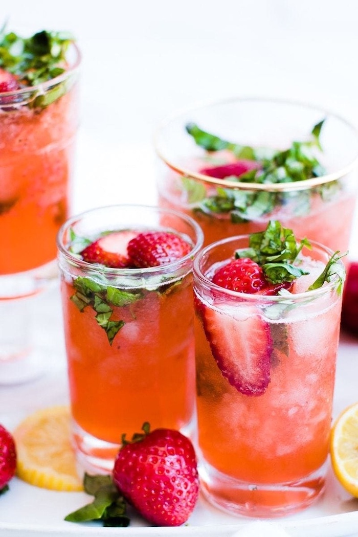 white background detox drinks glasses full of red juice with halved strawberries inside detox drinks lemon on the side
