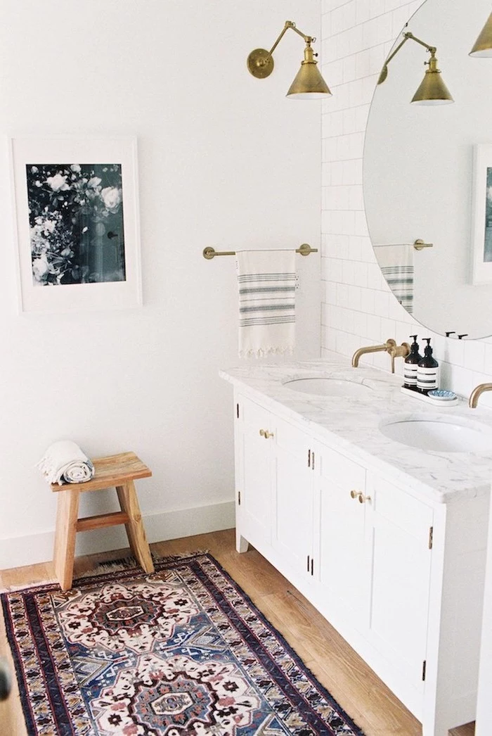 white vanity with two sinks large round mirror hanging above them on wall with white tiles modern farmhouse bathroom small rug on wooden floor