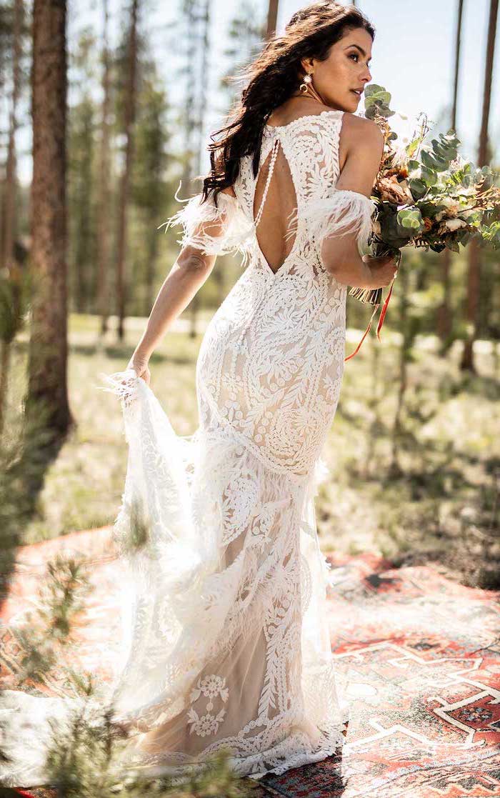 woman with long black wavy hair long sleeve boho wedding dresses wearing dress made of lace holding a large bouquet