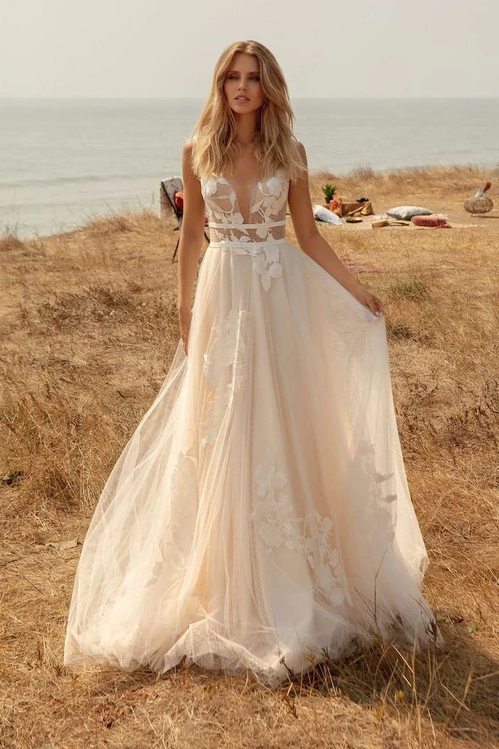 woman with long wavy blonde hair wearing flowy wedding dress made of tulle and lace photographed in a field