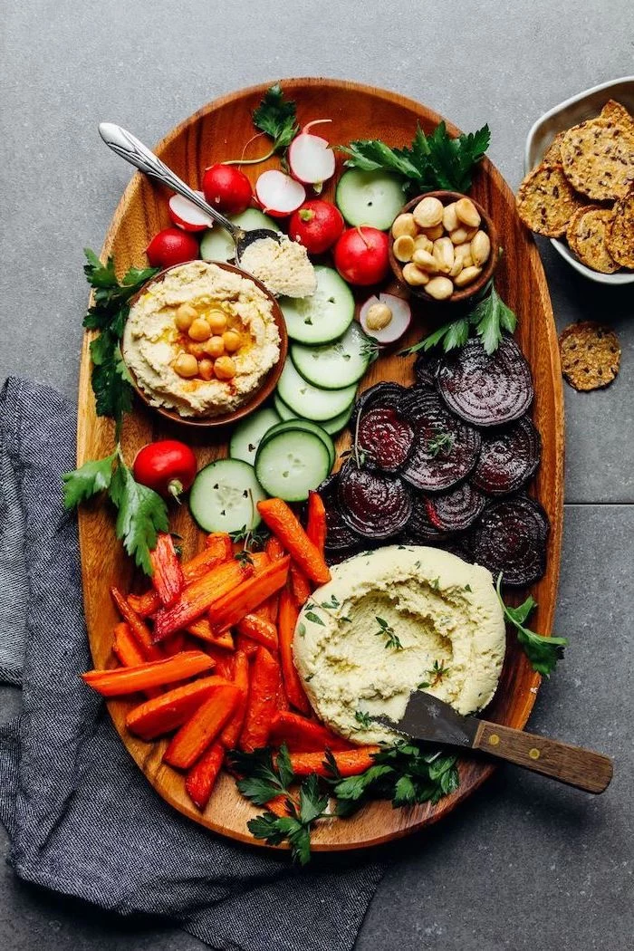 wooden tray full of different vegetables vegan appetizers two bowls of hummus garnished with parsley