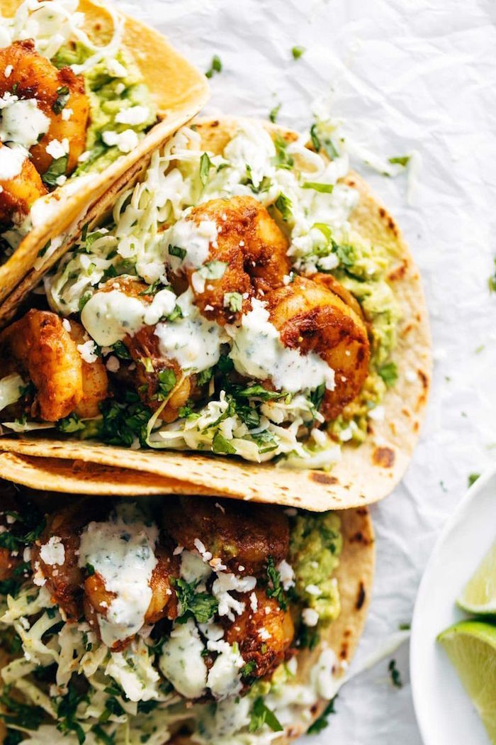 baked shrimp recipes three tacos arranged together on paper with shrimp chopped cabbage guacamole