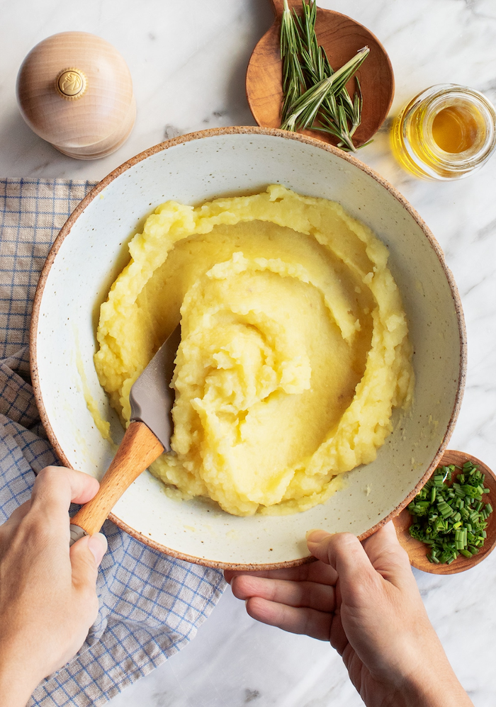 best thanksgiving side dishes mashed potatoes in white ceramic bowl being stirred with spatula other ingredients around it