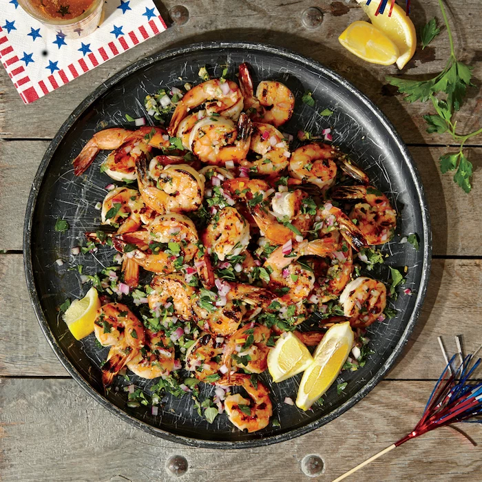 black ceramic plate with herbed grilled shrimp garlic shrimp recipe garnished with chopped parsley onion lemon wedges