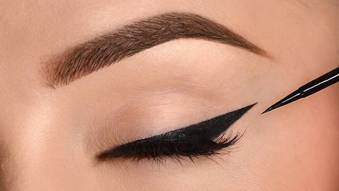 black eyeliner with sharp edge on closed eye winged eyeliner for hooded eyes close up photo of eye and thick eyebrow
