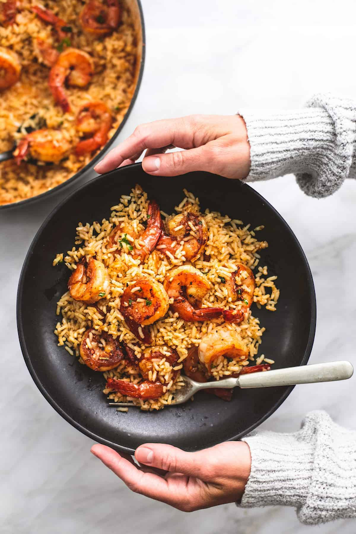 black plate filled with cajun shrimp and rice fork on the side shrimp dinner ideas held by two female arms wearing gray sleeves