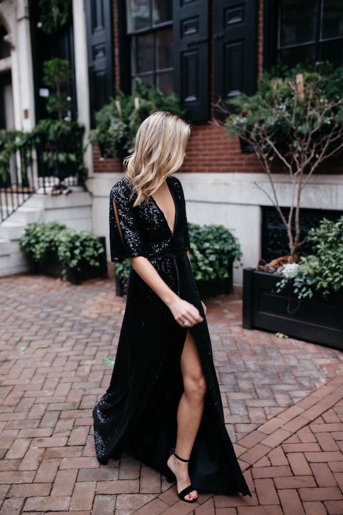 black sequin dress long with a slit worn by woman with blonde shoulder length hair winter wedding guest dresses walking on sidewalk