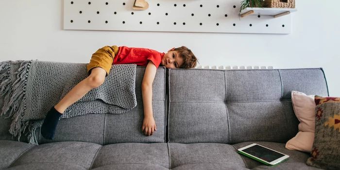 boy laying on the back of gray sofa wearing red t shirt mustard yellow pants indoor activities for kids
