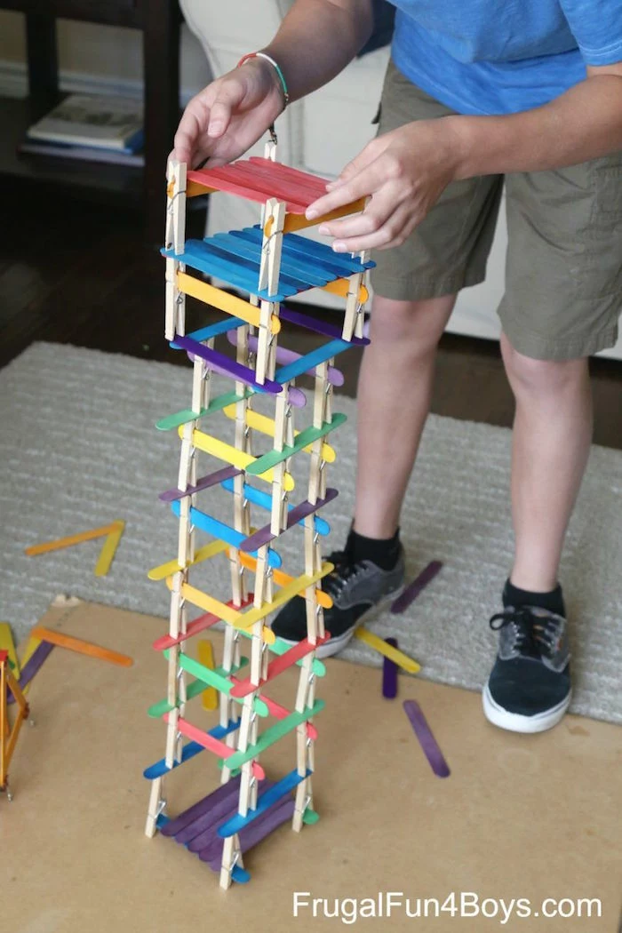 boy standing next to tower built out of clothespins and popsicle sticks craft ideas for kids in different colors