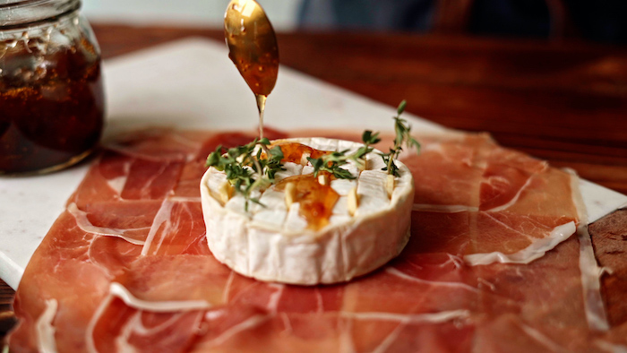 brie cheese covered with jam spread onto prosciutto slices thanksgiving dinner ideas placed on marble cutting board