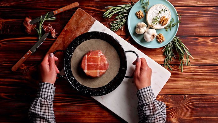 brie cheese covered with prosciutto placed on parchment paper lined baking sheet thanksgiving dinner ideas on wooden surface