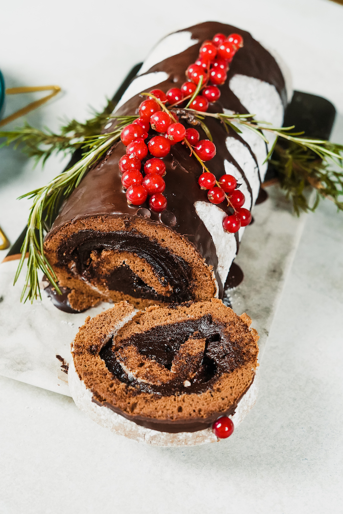 christmas dinner party ideas yule log dessert with a piece cut off decorated with chocolate cranberries rosemary branches