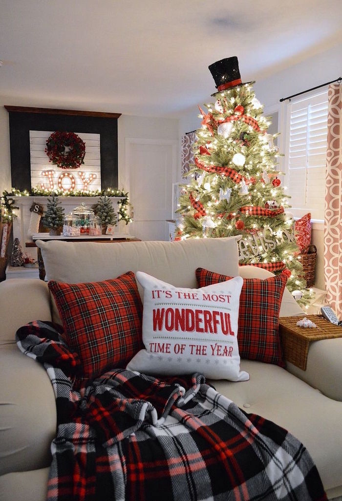 christmas tree decorations ideas 2020 with lots of lights red ribbon top hat tree topper standing behind white armchair with christmas throw pillows