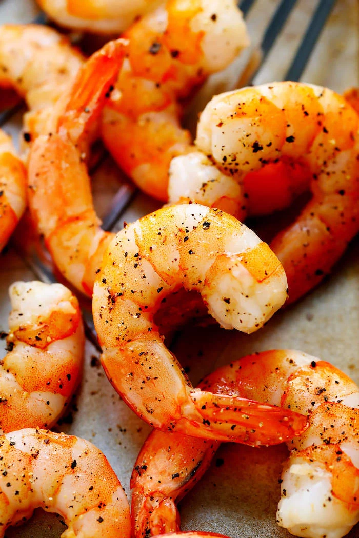 close up photo of baked shrimp garnished with herbs shrimp dinner ideas placed on paper lined baking sheet