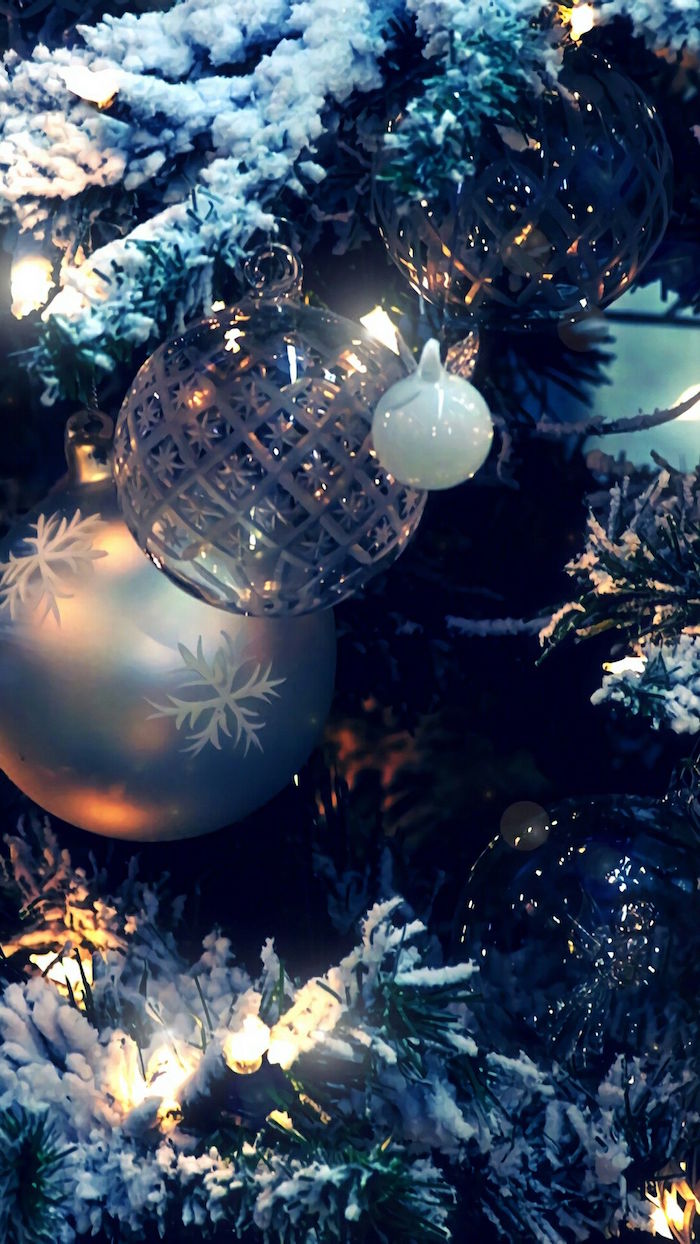 close up photo of decorated christmas tree covered with snow aesthetic christmas wallpaper silver baubles string of fairy lights