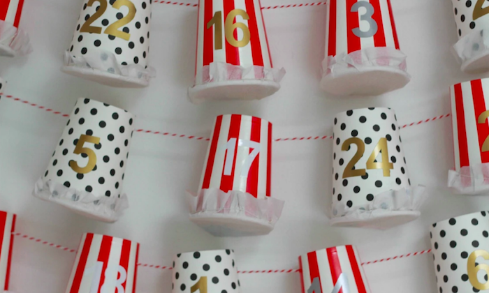 close up photo of paper cups white with black dots and red and white stripes homemade advent calendar labeled with numbers