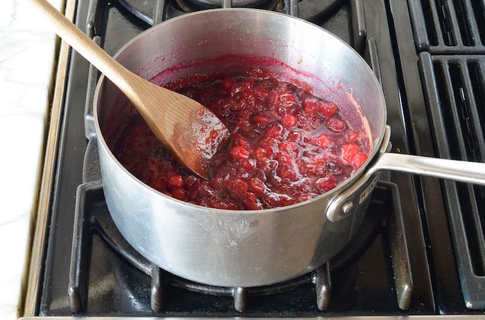 cranberry sauce cooking in metal pot on stove top christmas ham dinner being stirred with wooden spoon