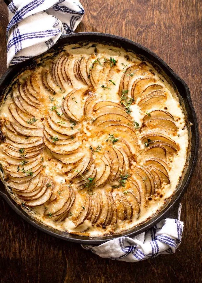 creamy potatoes au gratin best thanksgiving side dishes baked in black skillet placed on wooden surface