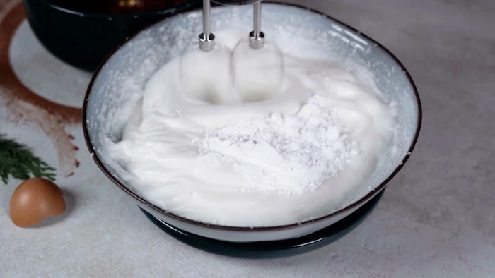 egg whites and powdered sugar being bitten together with a hand mixer christmas dinner party ideas in gray ceramic bowl