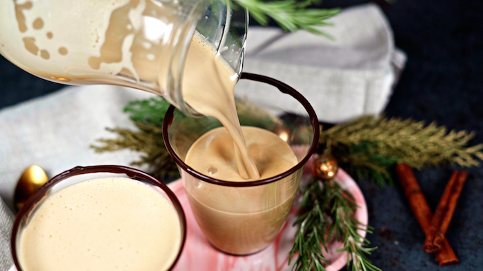 eggnog being poured into glass with chocolate on the rim from glass jug christmas dinner 2020