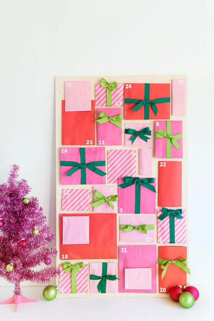 faux pink christmas tree next to unique advent calendars with paper bags filled with candy leaning on white wall