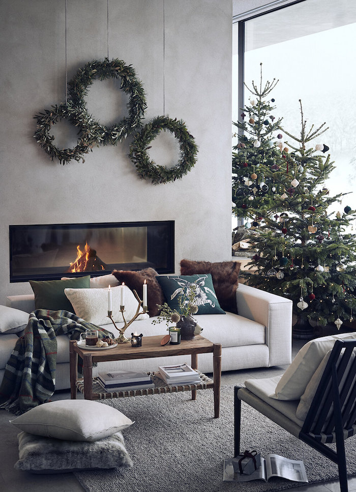 fireplace next to white sofa three wreaths above it christmas decorations 2020 two trees next to is with colorful ornaments
