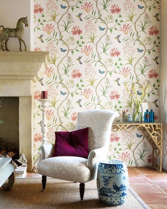fireplace with white armchair in front of it placed on white carpet vintage wallpaper with floral motifs on the wall next to the fireplace