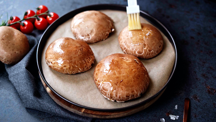 four portobello mushrooms covered with melted butter thanksgiving side dish recipes placed on paper lined baking dish