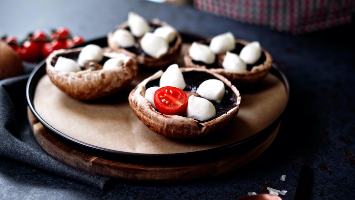 four portobello mushrooms stuffed with baby mozzarella cherry tomatoes thanksgiving side dish recipes placed on paper lined baking sheet