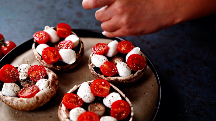 four portobello mushrroms placed on paper lined baking sheet thanksgiving side dish recipes stuffed with baby mozzarella cherry tomatoes