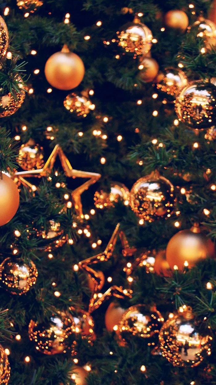 gold baubles and stars hanging on christmas tree decorated with fairy lights aesthetic christmas wallpaper close up photo