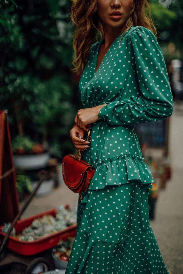 green dress with white dots and fringe long sleeves what to wear to a winter wedding worn by woman holding brown leather bag