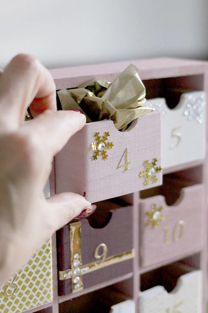 hand pulling out small box labeled with four painted in pink diy advent calendar ideas filled with candy and gold paper