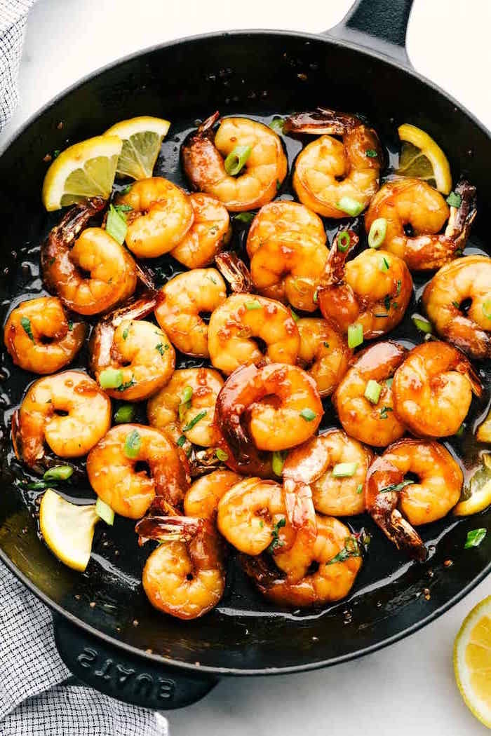 honey garlic butter shrimp cooked in black skillet garnished with chopped wild onion lemon slices placed on white surface