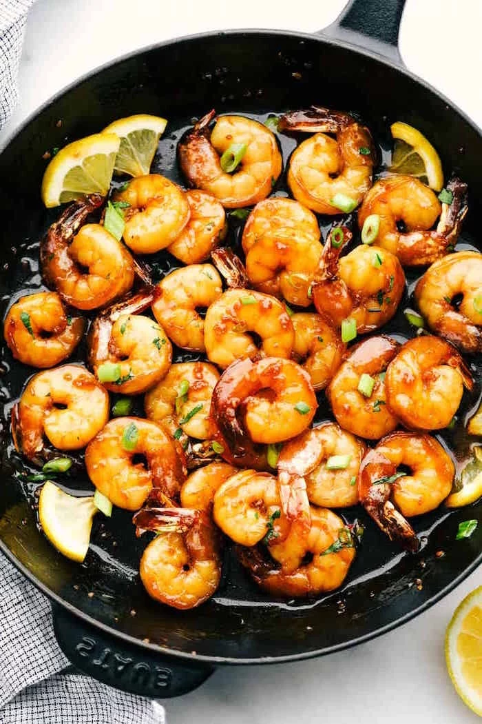 honey garlic butter shrimp cooked in black skillet garnished with chopped wild onion lemon slices placed on white surface