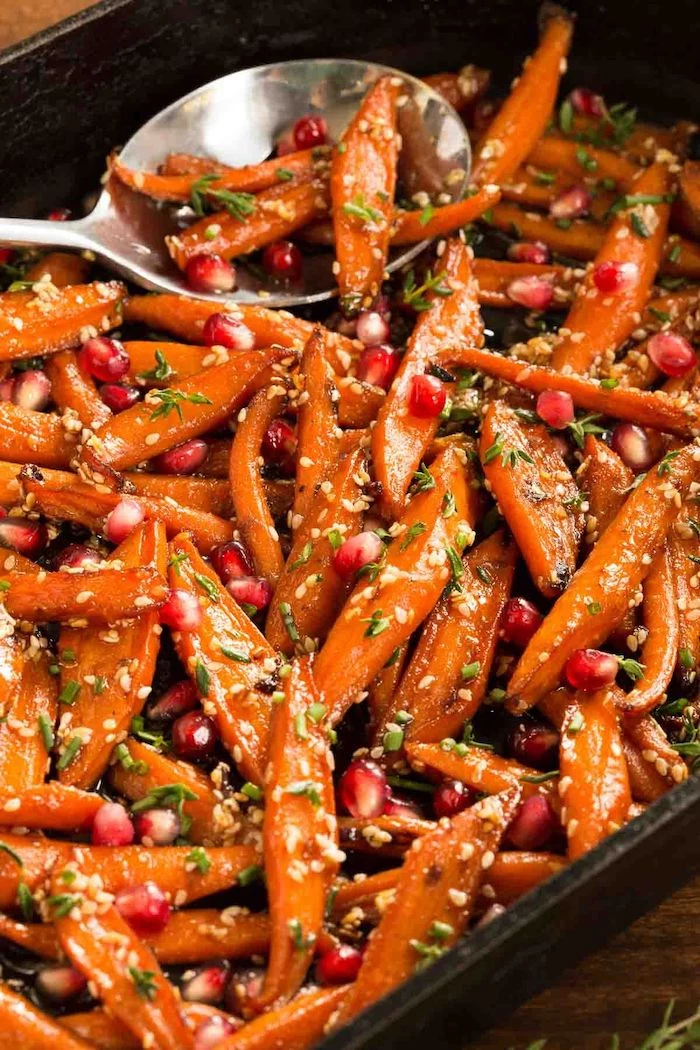 honey roasted carrots with pomegranate seeds inside black baking dish easy thanksgiving side dishes metal spoon