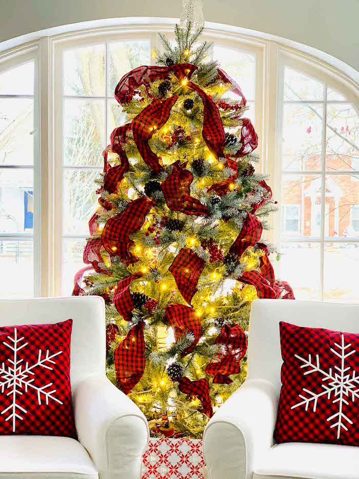 how to decorate a christmas tree real tree with lots of lights black and red plaid ribbon pinecones placed in front of window
