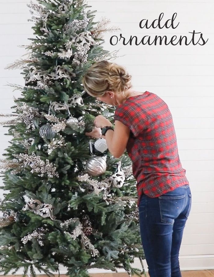 how to decorate a christmas tree with ribbon woman wearing red plaid shirt jeans adding ornaments to faux green tree