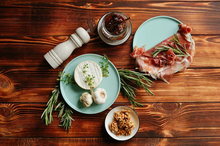 ingredients for baked brie thanksgiving food ideas prosciutto garlic walnuts jam thyme arranged on wooden surface