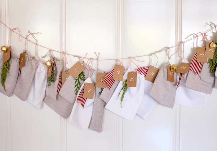lots of bags in gray and white hanging on a string on white wall diy advent calendar decorated with ribbons and mistletoe